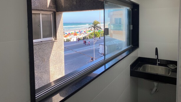A bathroom with a large window offering a view of a beach and ocean. - Apartment 30 meters from Praia do Forte beach - With beach view. (Cabo Frio)