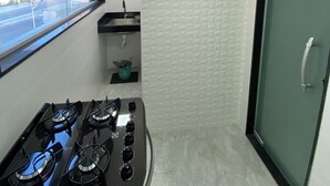 A compact kitchen with a gas stove, a window with a view of the outside, and a door leading to another room. - Apartment 30 meters from Praia do Forte beach - With beach view. (Cabo Frio)