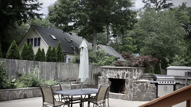 A patio with a stone fireplace, a grill, and a table with chairs.