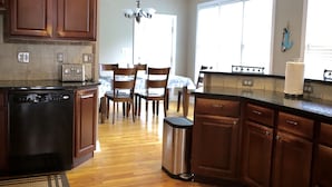 A kitchen with wooden cabinets, a dishwasher, a trash can, and a dining area with chairs and a table.