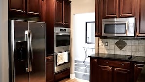 A kitchen with dark wooden cabinets, stainless steel appliances including a refrigerator, oven, and microwave, and a tiled backsplash.