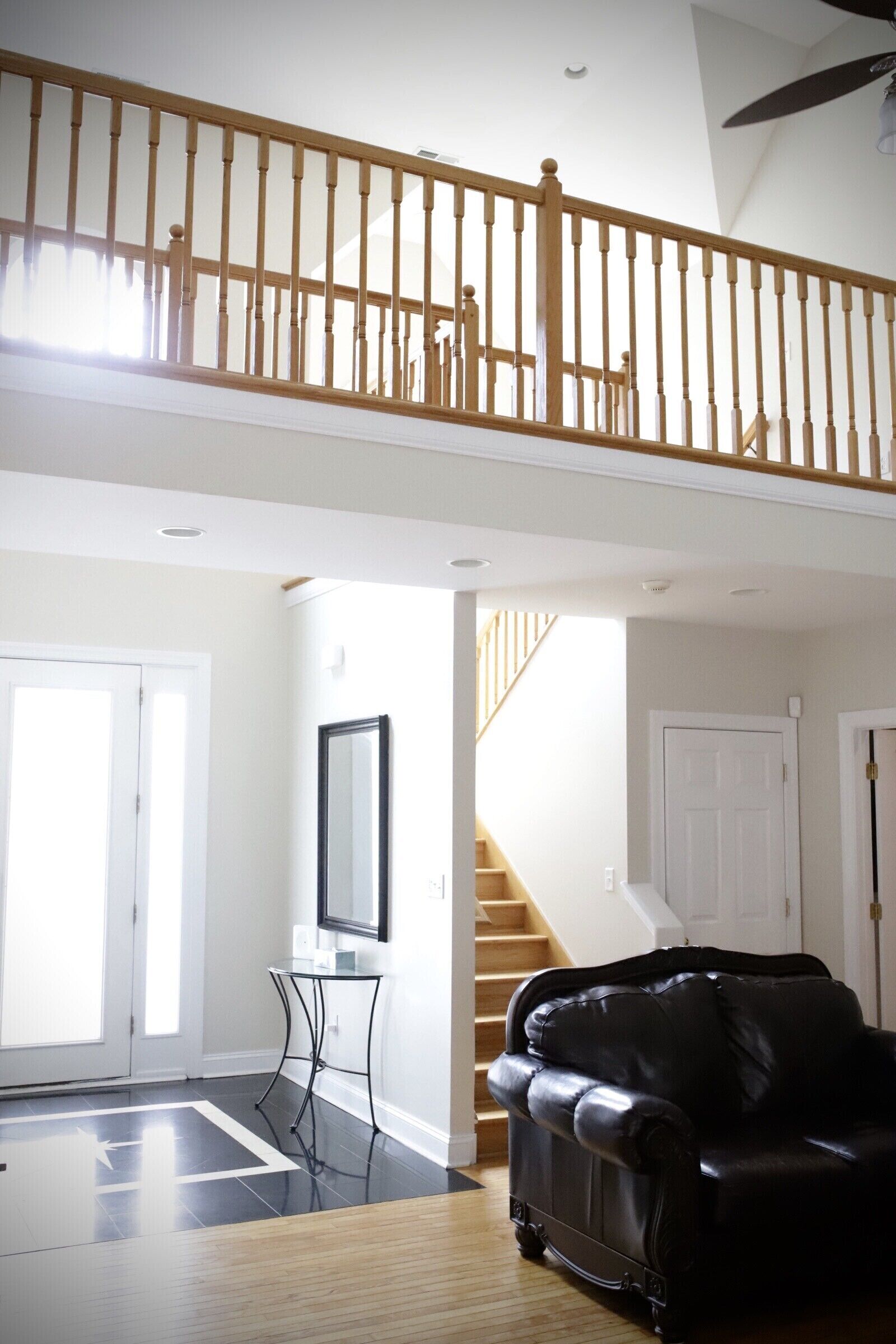 Un salon spacieux avec un canapé en cuir noir, un escalier en bois et un ventilateur de plafond.