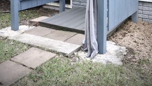 A blue wooden gate with a grey curtain, leading to a house with white siding and a window.