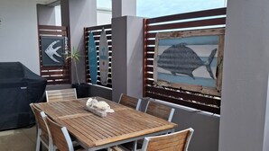 A patio with a wooden table and chairs, a grill, and a view of the beach. - Gillian's on the beachfront Port MacDonnell, the best view in town. (Port MacDonnell)