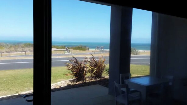 A view from a window overlooking a beach with a road, a playground, and some vegetation. - Gillian's on the beachfront Port MacDonnell, the best view in town. (Port MacDonnell)
