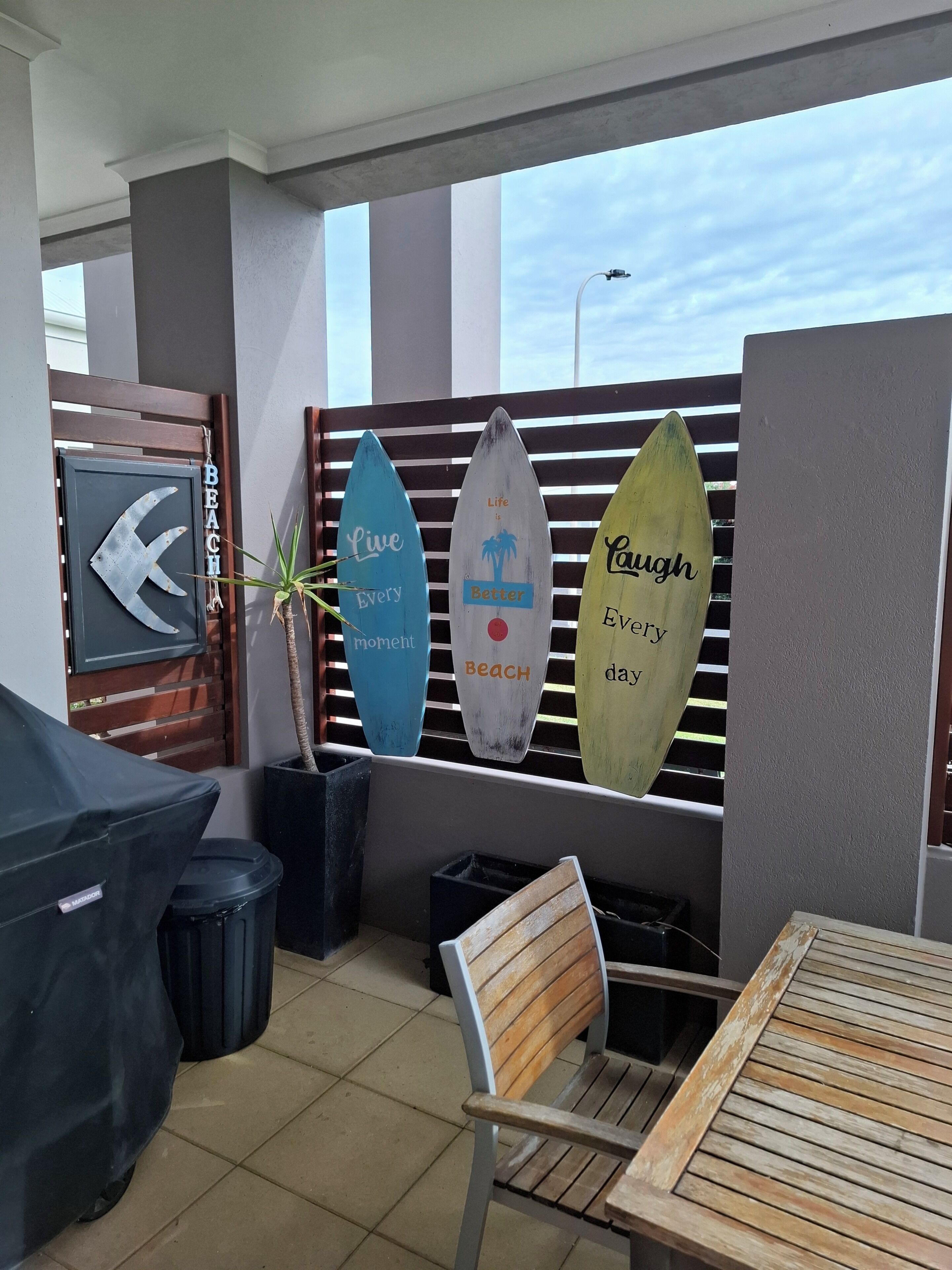 Ein Patio mit Tisch, Stühlen, einem Grill und Surfbrettern mit motivierenden Sprüchen.