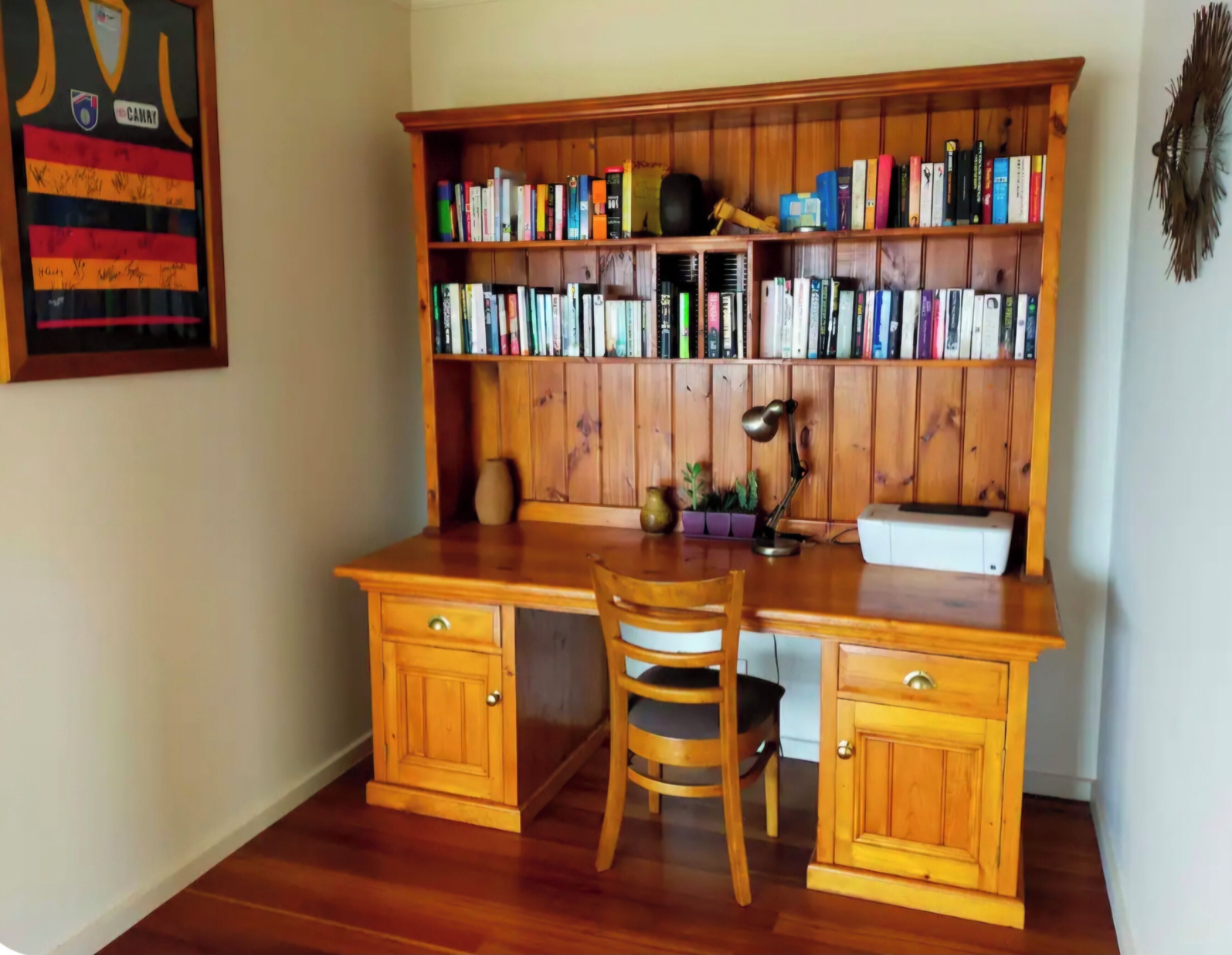 A wooden desk with a chair, a bookshelf filled with books, and a desk lamp.