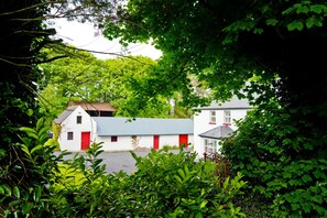 Un edificio blanco con puertas y ventanas rojas, rodeado de un follaje verde exuberante.