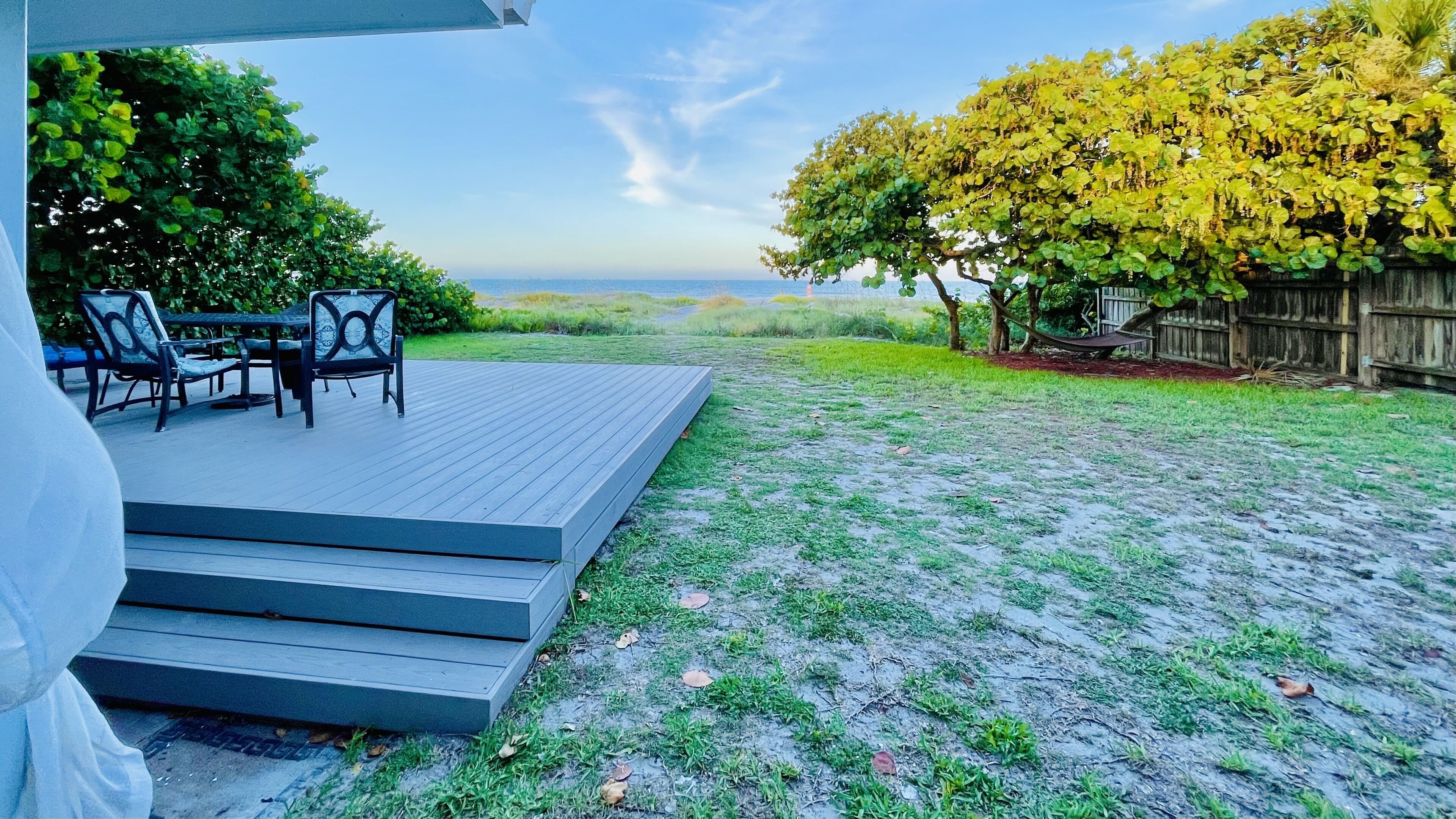 A deck with outdoor furniture, a wooden fence, and a view of the ocean.
