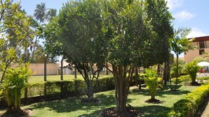 Un giardino curato con diversi alberi e arbusti, un'area recintata e un edificio sullo sfondo.