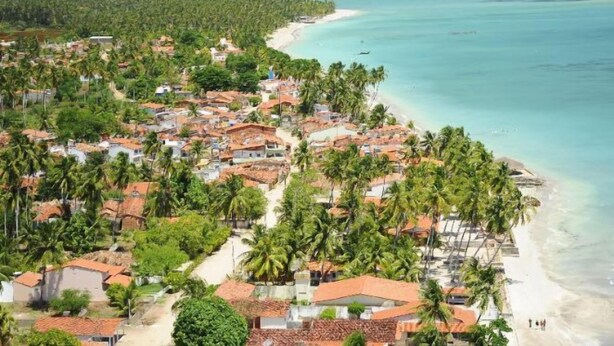Un villaggio costiero con case e palme, una spiaggia e una vista limpida sull'oceano.