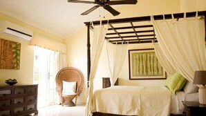 Una camera da letto con un letto, una ventola a soffitto, una sedia, una cassettiera e una finestra con tende.
