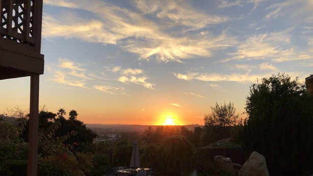 Zonsondergang boven een zwembad met terrasmeubilair.