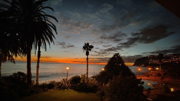 Une vue sur le coucher de soleil, avec des palmiers, une piscine et une plage illuminée.