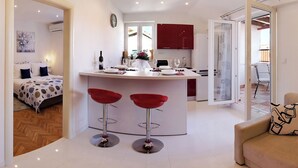 Una cocina moderna con armarios rojos, una isla central con dos taburetes rojos y una zona de comedor con mesa y sillas blancas.