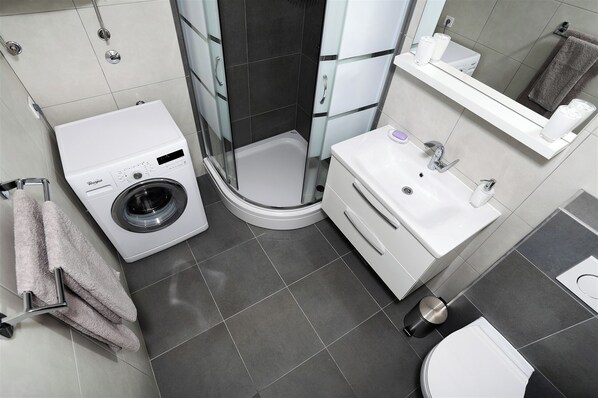 A modern bathroom with a washing machine, a shower, a sink, and a toilet.