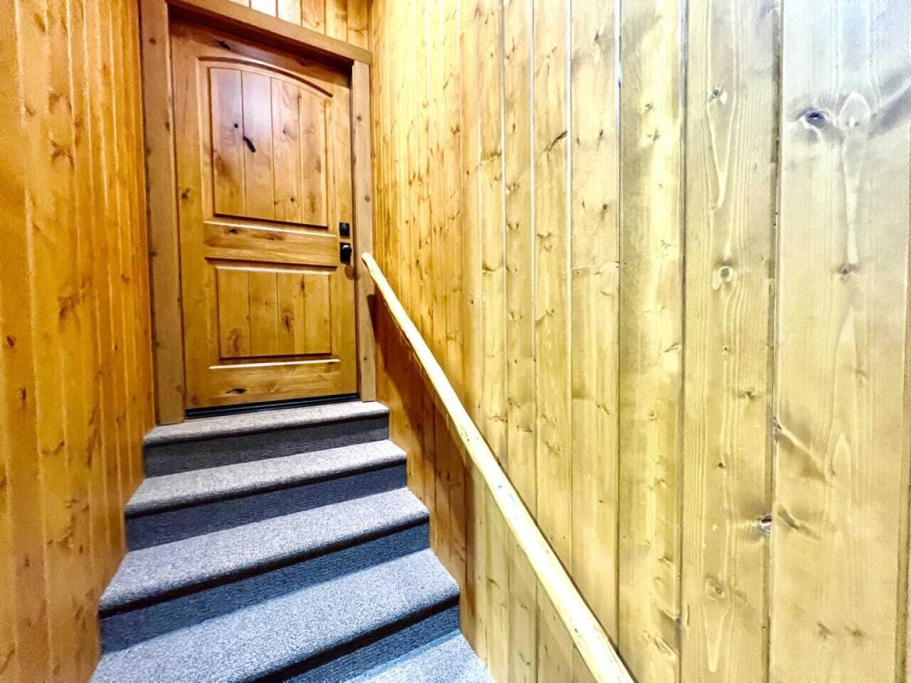 A wooden staircase with a carpeted landing leading to a wooden door.
