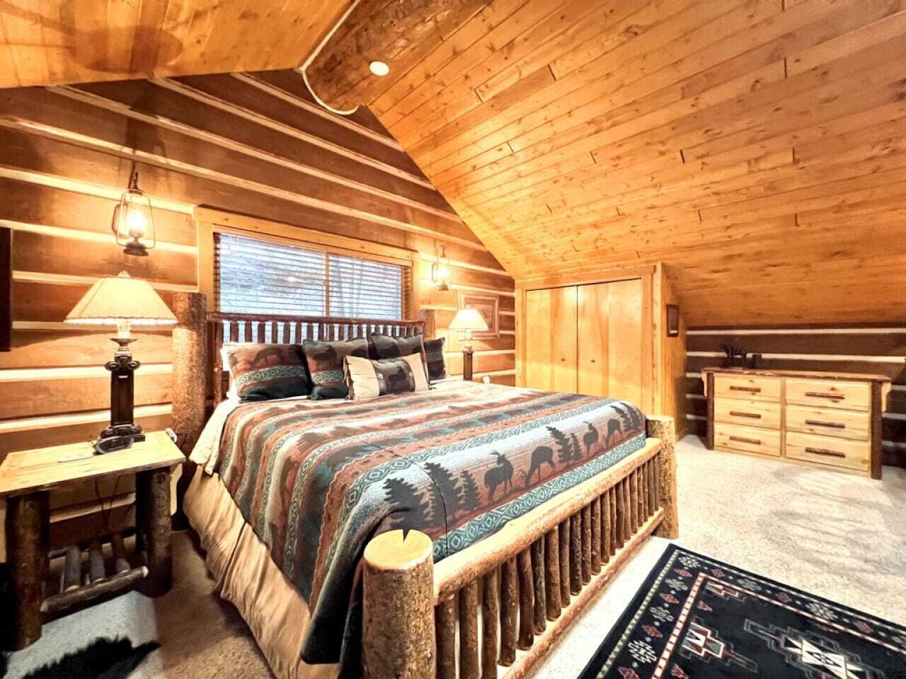 Un dormitori de cabana de fusta amb un llit gran, un reposacapses de fusta i un sostre de fusta rústica.