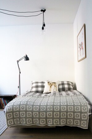 Un letto rifatto con una coperta a quadri, una lampada da scrivania nera e un quadro appeso al muro.