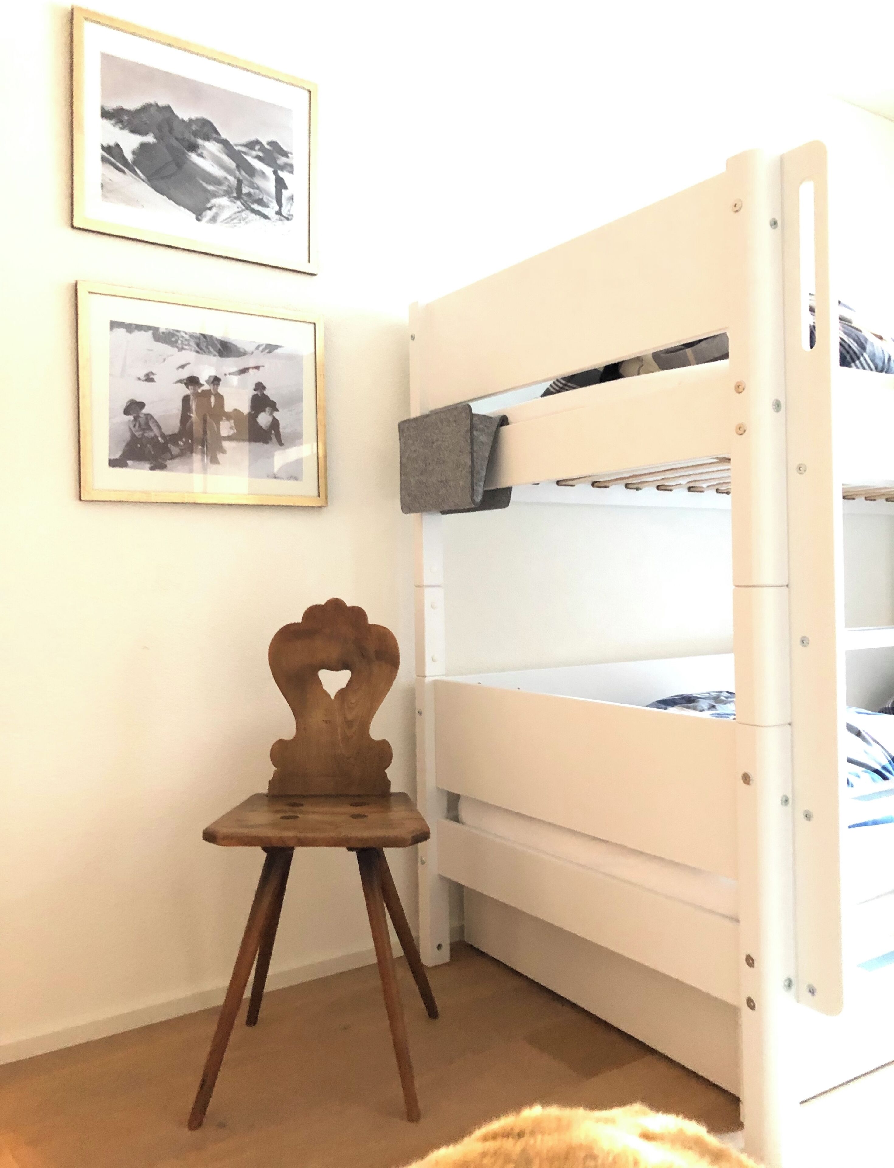 Una cama litera con una silla de madera en una habitación con dos cuadros en la pared.