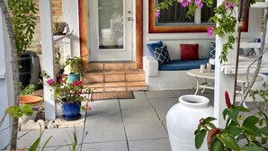 A covered porch with a door, a blue sofa with patterned cushions, and various potted plants.