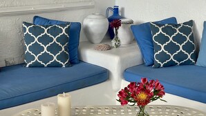 A modern living room with blue sofas, patterned cushions, a white decorative wall, and a round table with a geometric design.