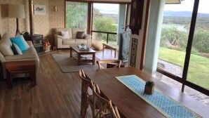 Uma sala de estar ampla com piso de madeira, um conjunto de sofás, uma mesa de centro e uma mesa de jantar com cadeiras.