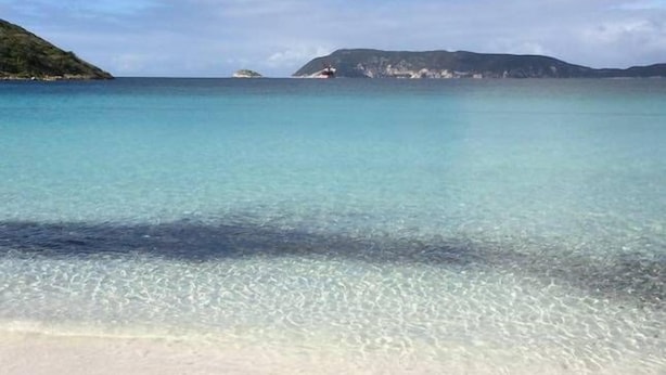 Uma praia com águas turquesa cristalinas, margem arenosa e ilhas ao longe.