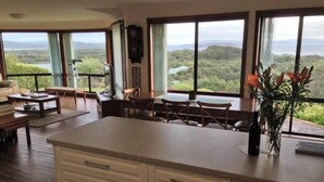 Uma cozinha ampla com uma ilha grande, armários de madeira e vista para uma paisagem exuberante através de grandes janelas.
