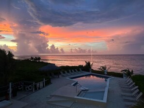A pool area with lounge chairs and a view of the ocean at sunset. - Paradise Found Oceanfront Condo - Flexible Cancellation (Grand Cayman)