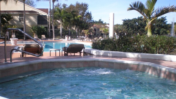A hot tub area with a pool, lounge chairs, and palm trees. - Spacious one bedroom-one bath condo (Naples)