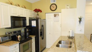 A kitchen with white cabinets, a stainless steel refrigerator, a microwave, and an oven. - Spacious one bedroom-one bath condo (Naples)