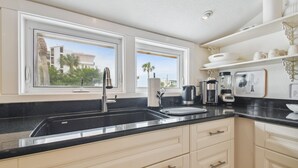 A modern kitchen with a black countertop, white cabinets, and a window with a view of palm trees and buildings. - White beaches, walk to restaurants and shops! Family vacation /Romantic getaway! (Clearwater)
