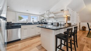 A modern kitchen with white cabinets, a black countertop, and a central island with bar stools. - White beaches, walk to restaurants and shops! Family vacation /Romantic getaway! (Clearwater)