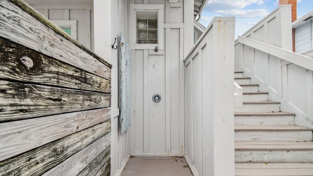 A narrow wooden pathway leading to a white door with a small window, flanked by a white fence and a staircase. - White beaches, walk to restaurants and shops! Family vacation /Romantic getaway! (Clearwater)