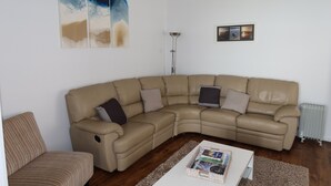 A living room with a beige sectional sofa, a striped armchair, a coffee table with magazines, a floor lamp, and abstract wall art. - Ducks Bungalow- Lake Macquarie (Marks Point)