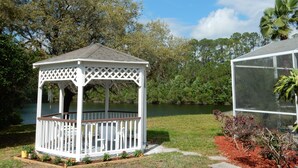 A gazebo with a lattice roof and a fenced deck, situated next to a pond and a greenhouse. - Private Pool + Heated Hot Tub | Lake View (Davenport)