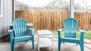 Two turquoise chairs and a small white table on a concrete patio with a wooden fence in the background.