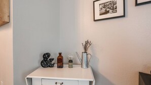 Een wit bureau met een lade, een vintage Edisonlamp, een metalen vaas met gedroogde bloemen en een zwart-wit fotolijst aan de muur.