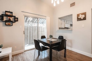 A dining area with a table, chairs, and a small plant. There is a sliding glass door leading to a patio.
