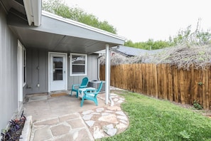 Une terrasse couverte avec un sol en pierre, deux chaises turquoise et une petite table.
