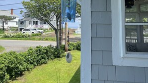 A house with a porch, a hanging wind chime, and a view of the street and neighboring houses. - Beautiful Roomy Beach House...See and Hear the Ocean Waves (Wells)