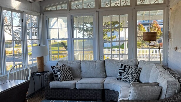 A cozy room with a large sectional sofa, a dining table, and a wicker chair. - Beautiful Roomy Beach House...See and Hear the Ocean Waves (Wells)