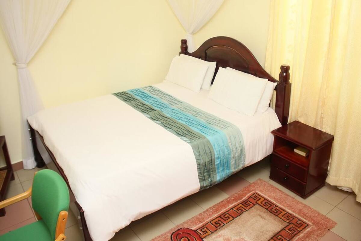 A neatly made bed with a wooden headboard, a bedside table with a book, and a green chair.