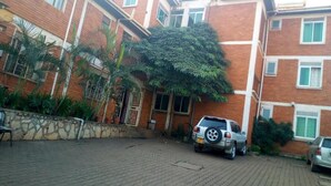 Un edificio de varios pisos con fachada de ladrillo, un patio empedrado y coches estacionados.