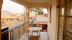 Un balcón con una mesa y sillas, con vista a una calle con edificios y un árbol.