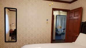 Een hotelkamer met een bed, een bureau met een lamp, een spiegel en een deur naar een andere kamer.