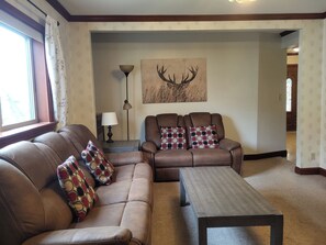 A living room with a brown leather sofa, a matching armchair, and a wooden coffee table. There is a lamp and a deer antler wall art piece. - A beautiful 3BR Apartment near Harvard and MIT. (Cambridge)