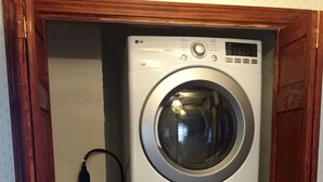 Een gestapelde wasmachine en droger in een wasserette met een houten deurkozijn.
