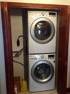A stacked washer and dryer unit in a laundry room with a wooden door frame. - A beautiful 3BR Apartment near Harvard and MIT. (Cambridge)